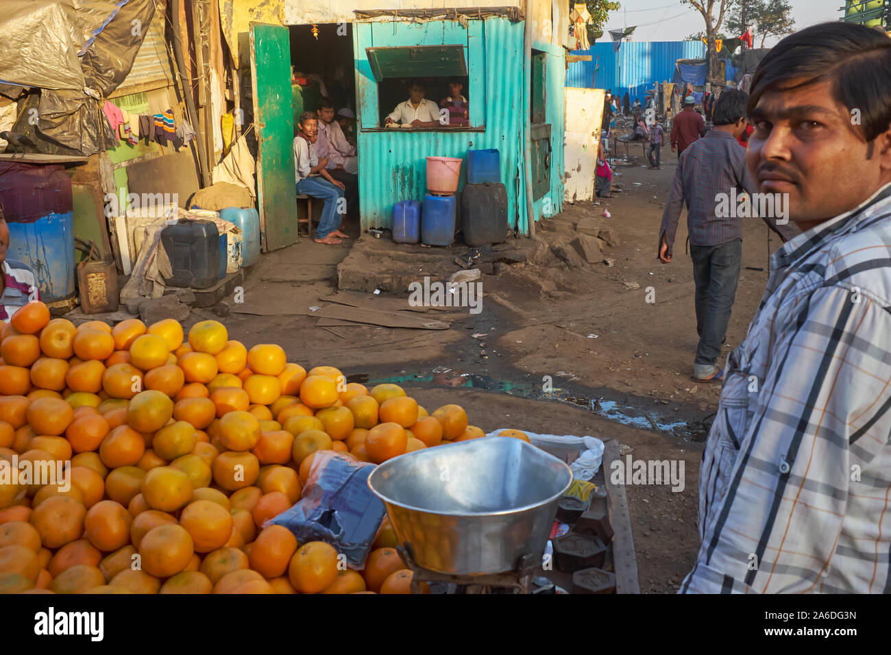 An orange vendor with his trolley passes a tin shack serving as food shop in Darukhana slum area in Mazgaon (Mazagaon), Mumbai, India Stock Photo