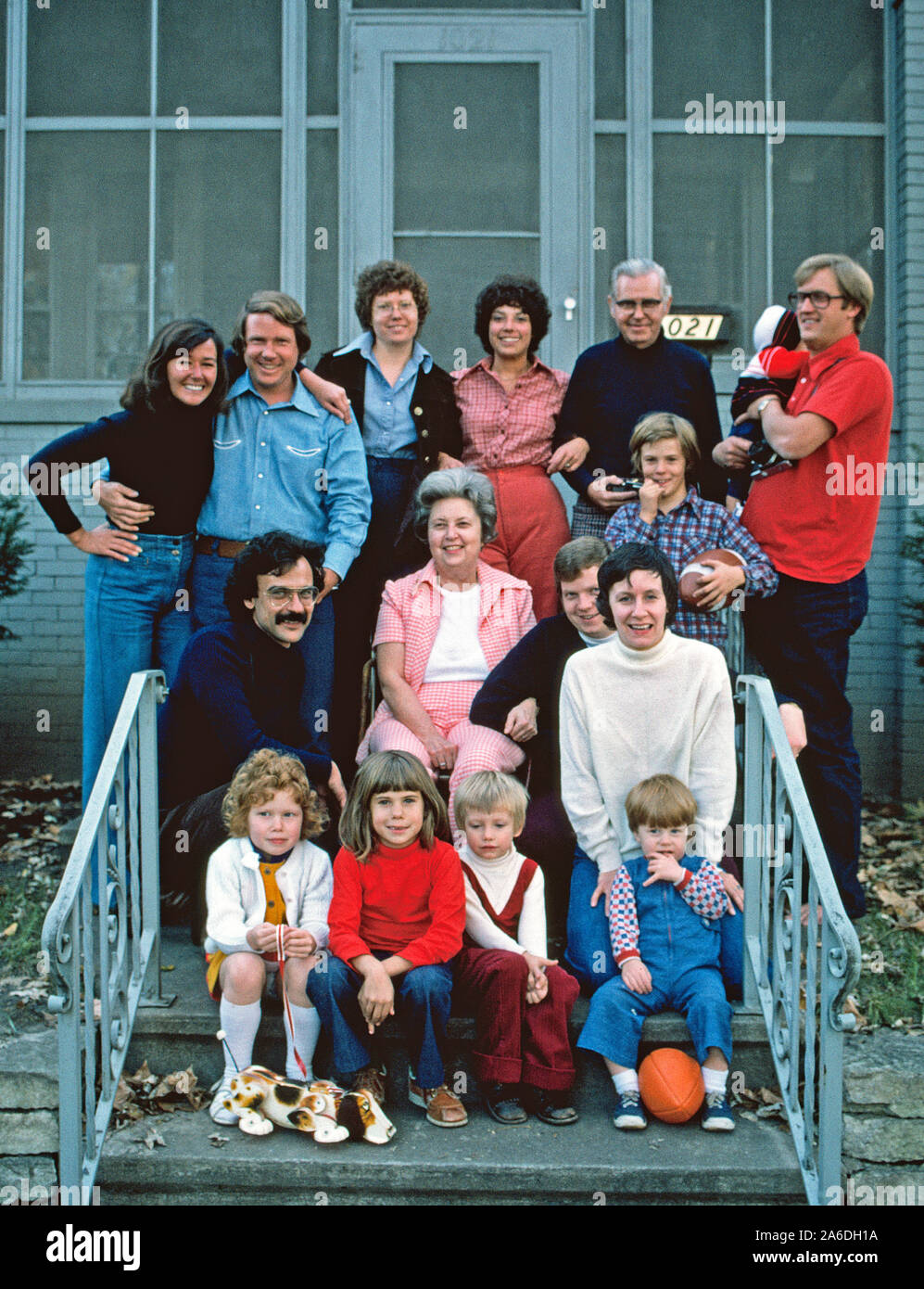 Sixteen members of an American family pose outdoors in 1975 on the front steps of the family home. The elderly gray-haired couple show off their two sons and two daughters with their wives and husbands and six grandchildren (including a sleeping baby hidden in the back row). The occasion was the family's annual reunion at Christmastime. Notice the 1970s hairstyles and clothing. Stock Photo