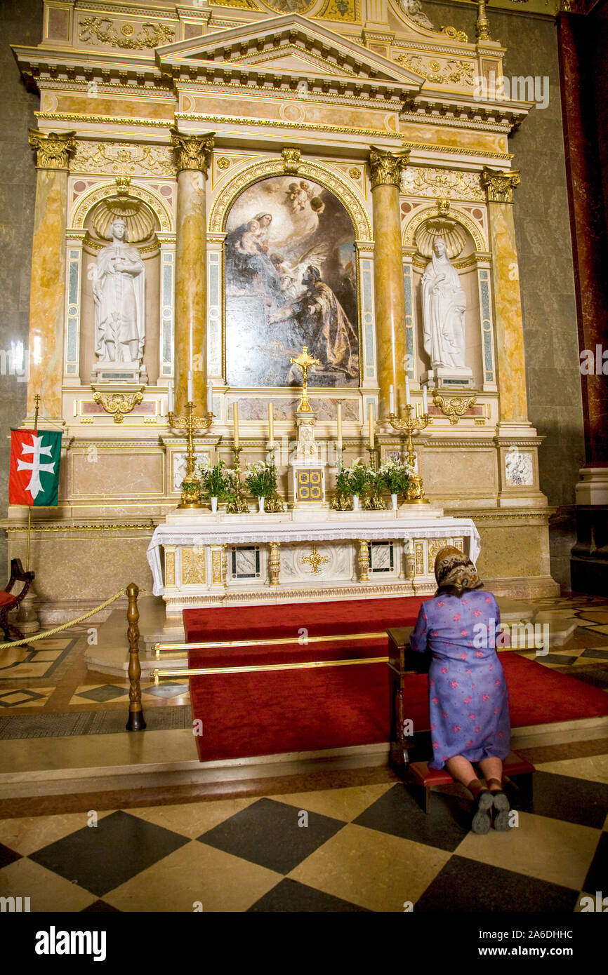 Woman kneeling in prayer beneath a painting by Gyula Benczur in St. Stephen's Basilica ( Szent Istvan Bazilika) in Budapest. Stock Photo