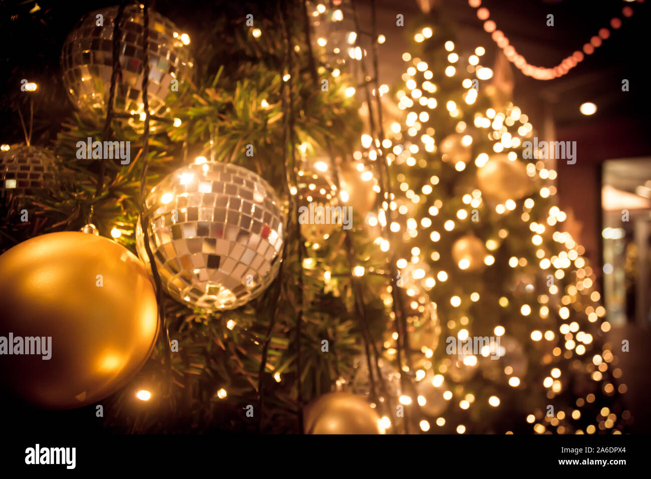 Christmas tree with gold ball and bokeh lights background. Xmas abstract close up with glowing decorations outdoors. Stock Photo