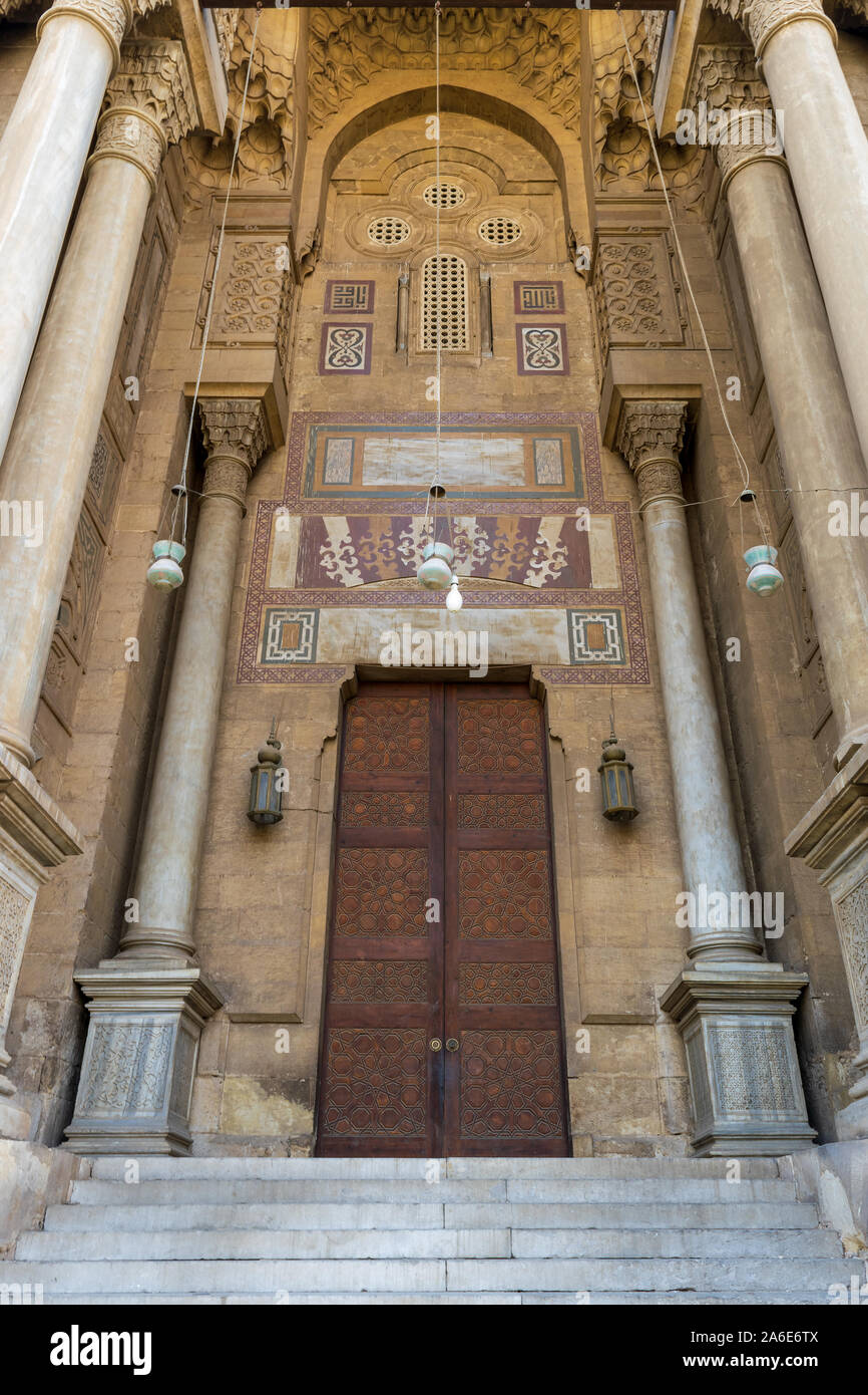 Side entrance of al Rifai Mosque, old decorated bricks stone wall with arabesque decorated wooden door framed by marble engraved cylindrical columns, Medieval Cairo Egypt Stock Photo