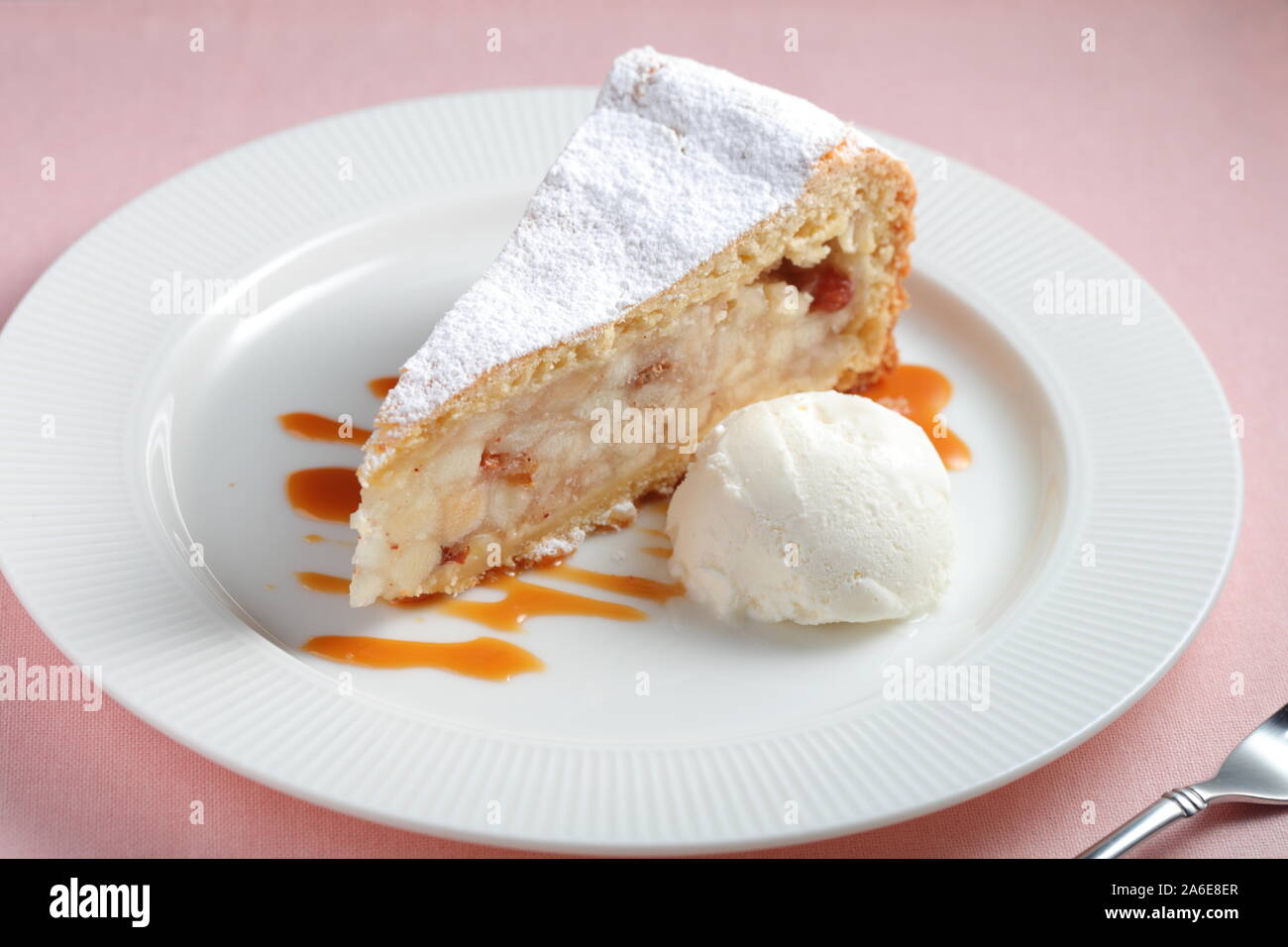 Slice of apple strudel topped with powdered sugar and a ball of vanilla ice cream on a plate decorated with caramel sauce Stock Photo