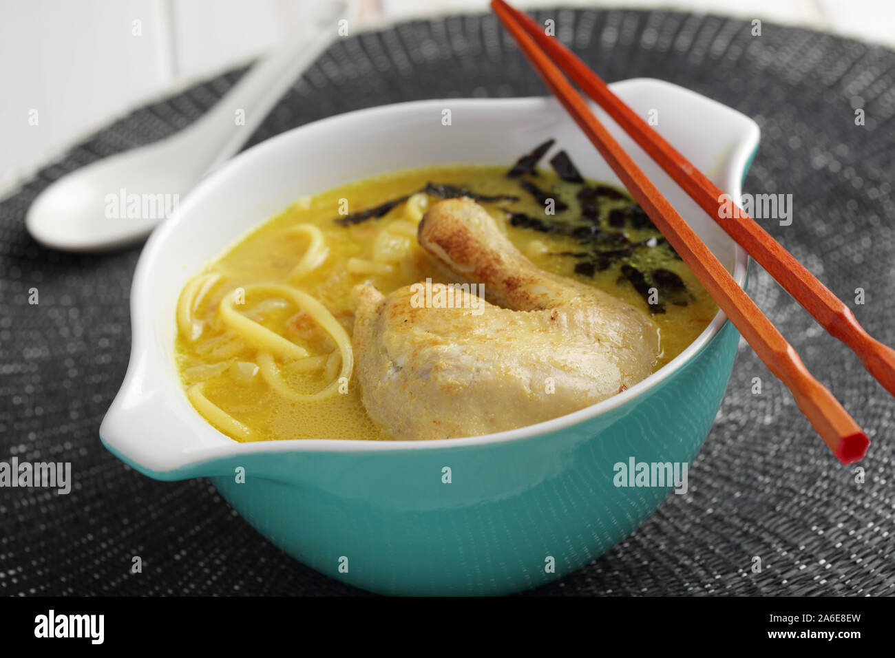 Bowl of chicken coconut milk soup with pasta, curry, and nori Stock Photo