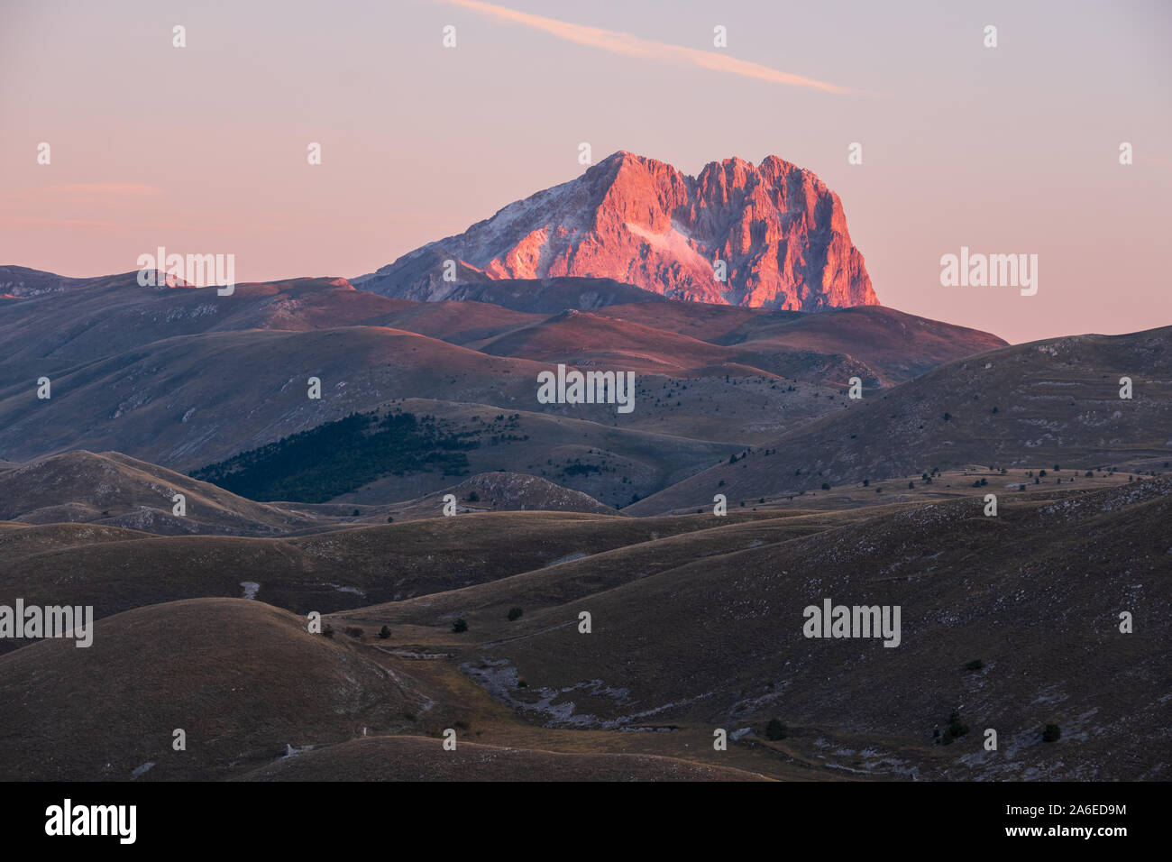 Mountain Corno Grande on horizon behind barren and rural landscape glowing pink in light of sunrise, Abruzzo, Italy Stock Photo