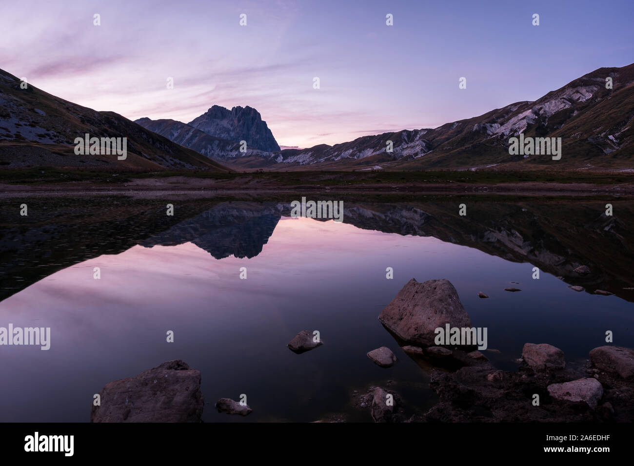 Sunset on Campo imperatore at small lake Laghetto Pietranzoni with stones in foreground beautiful reflection of mountain Corno Grande in background, A Stock Photo