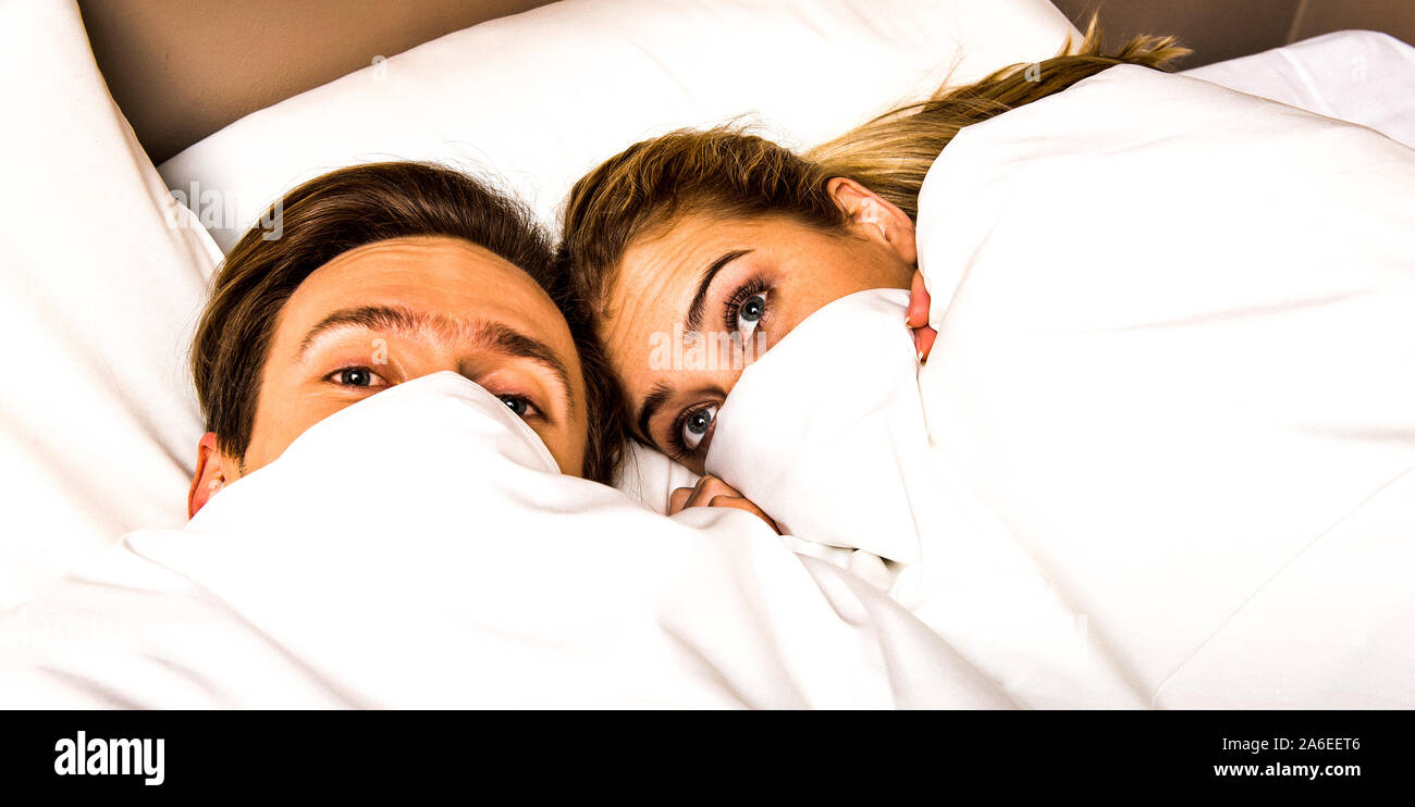 Married couple hiding in bed under duvet in morning time. Relax after awaking. Stock Photo