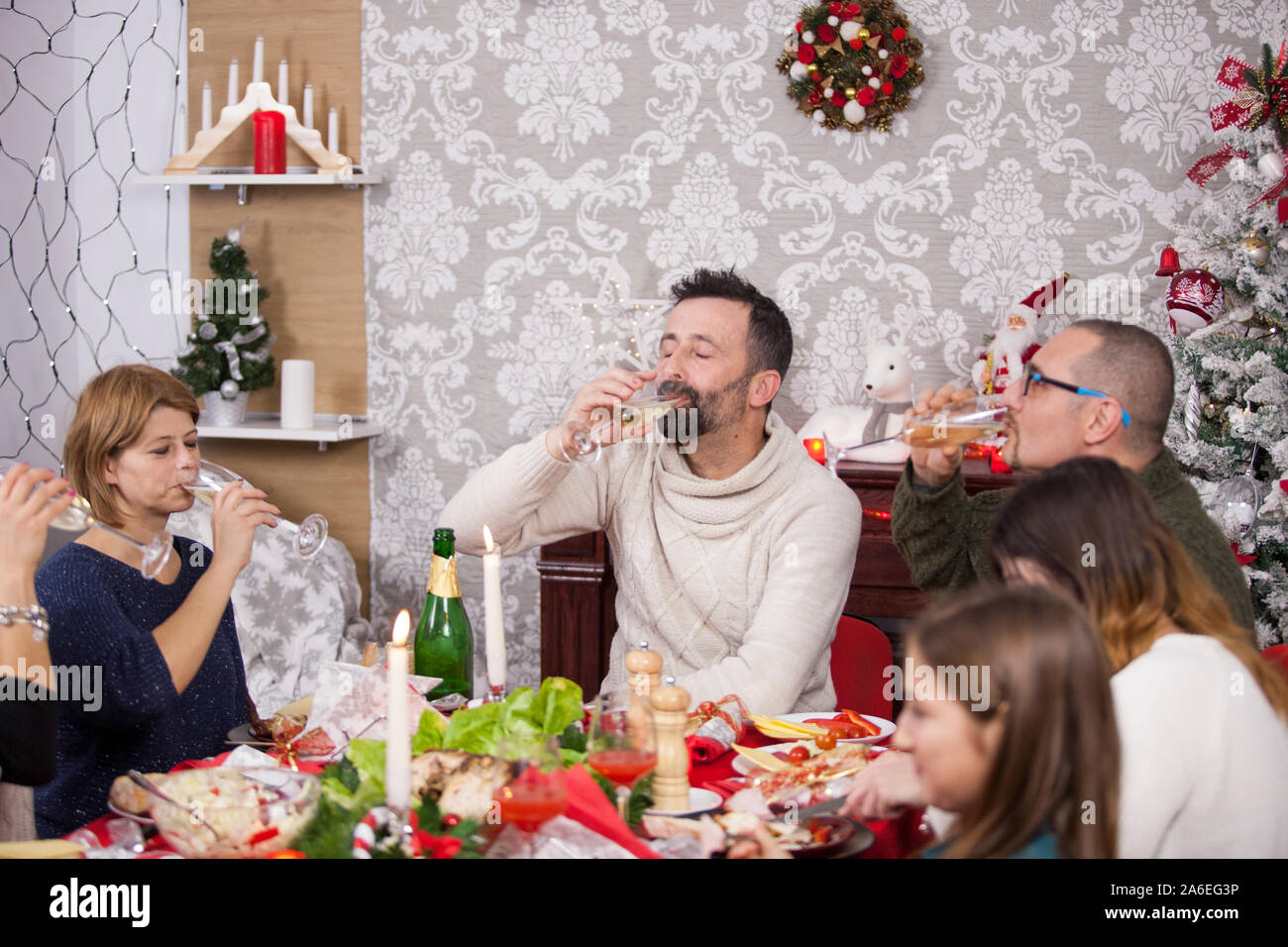 Family gathered around the table for traditional christmas celebration drinking a glass of champagne. Christmas decoration on the table. Children enjoying christmas feast. Stock Photo