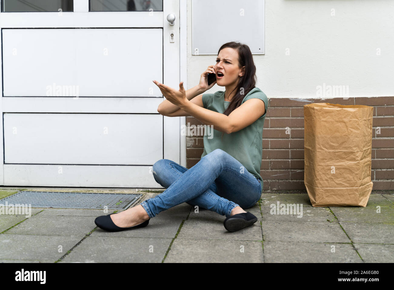 An Afraid Young Woman Sitting Outside The Door Talking On Mobilephone Stock Photo