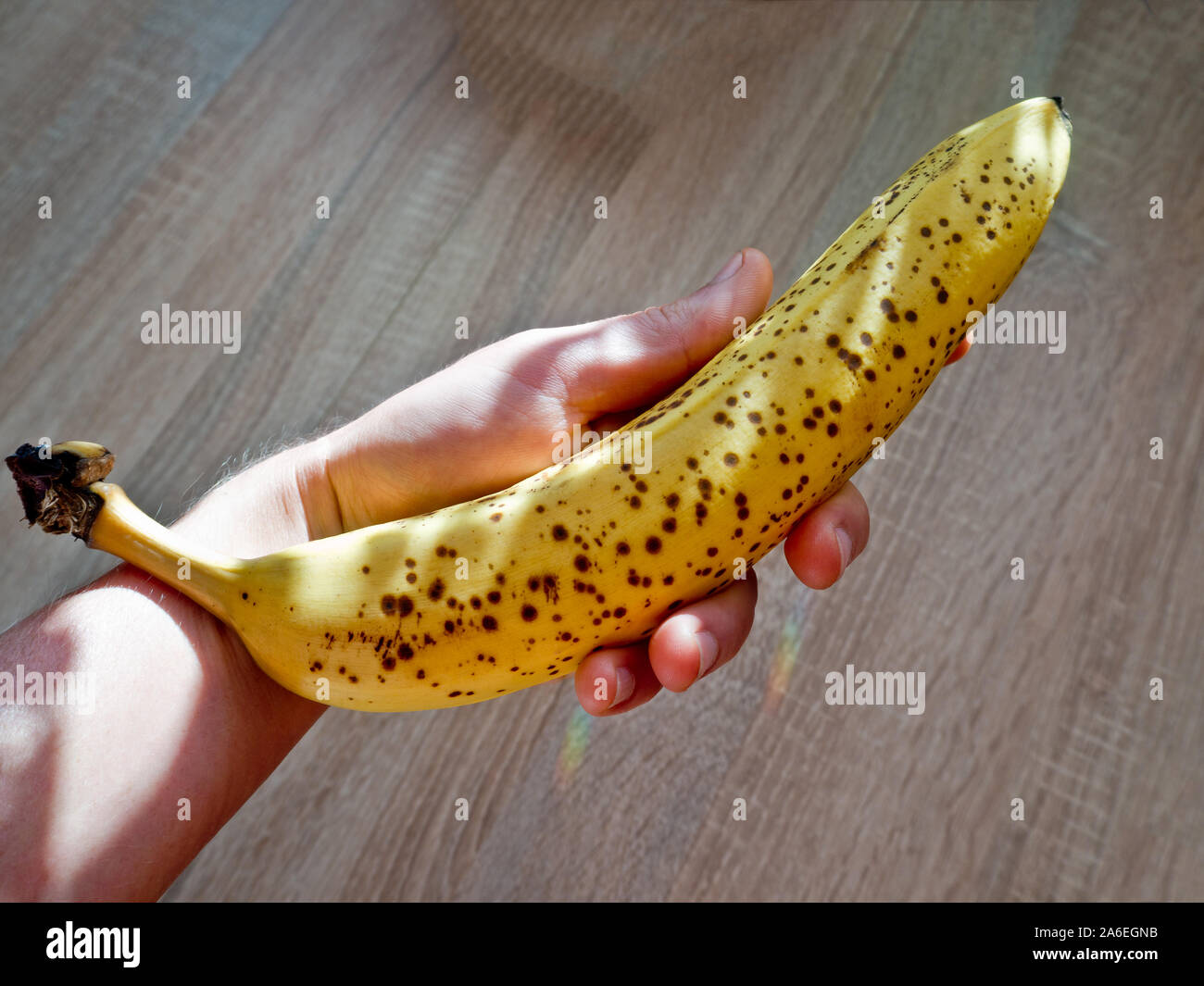 A ripe banana in the hand with wooden background. Stock Photo