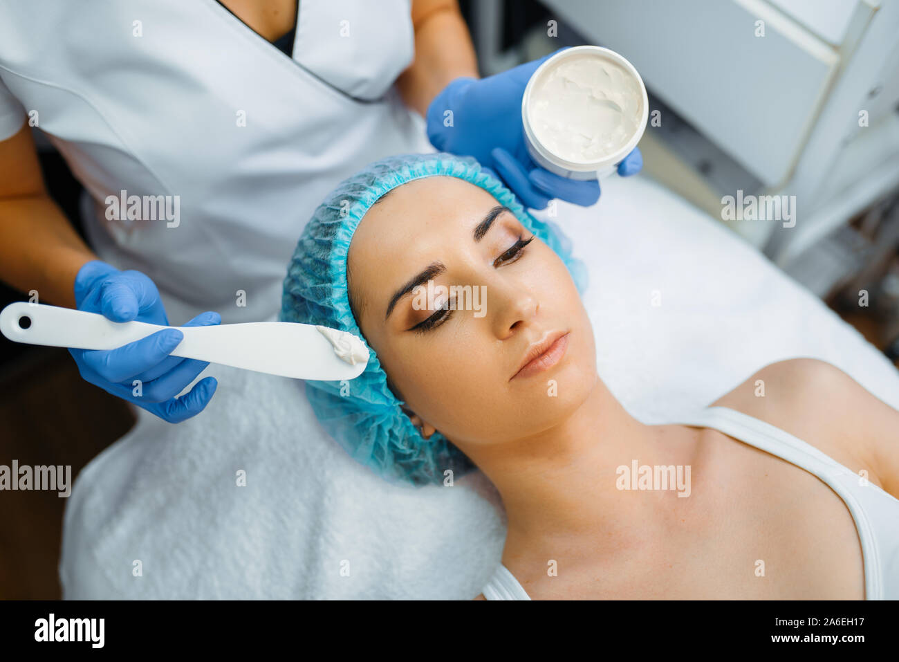 Cosmetician applies the cream to patient's face Stock Photo