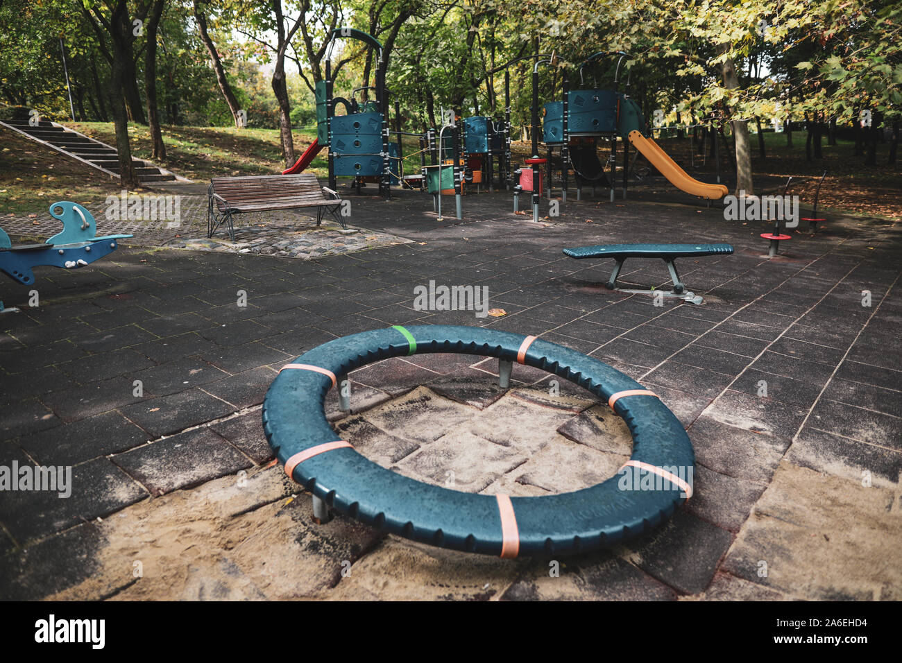 Colorful children's playground with slides, swings and other objects in a public park with many trees around and no people Stock Photo