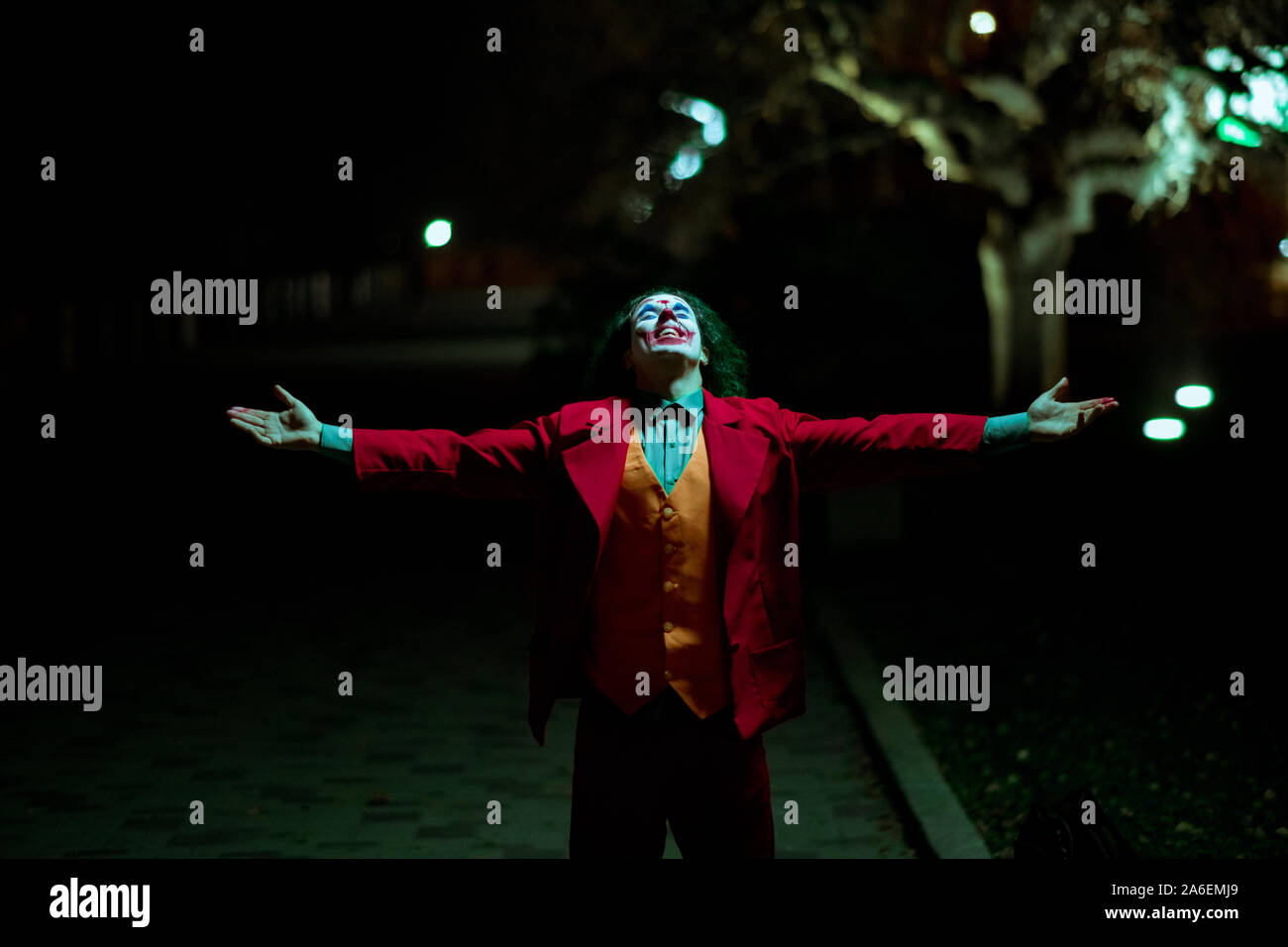 Cosplayer in the image of a crazy clown walks at nigth city. Stock Photo