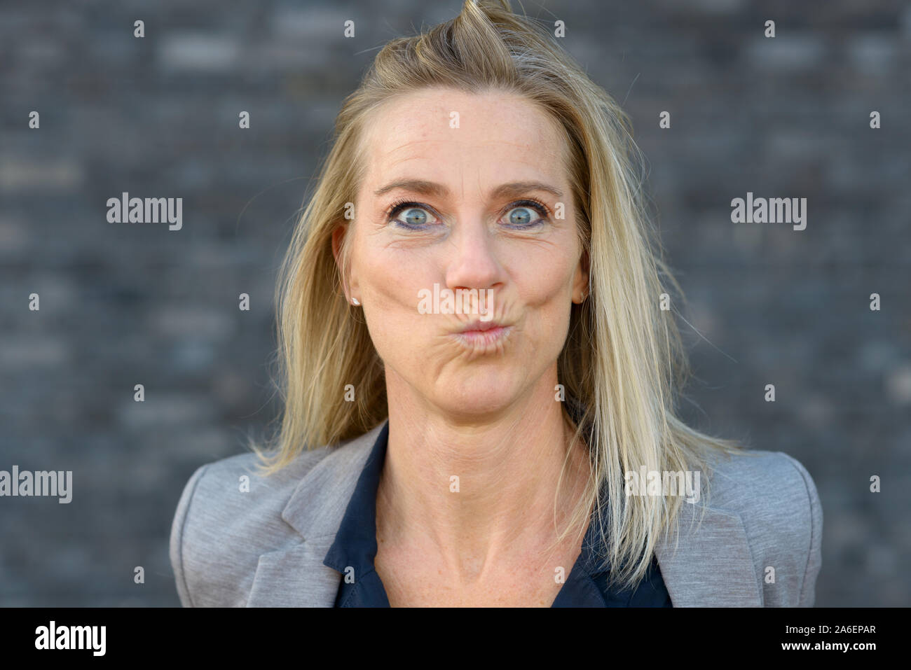 Front view portrait of a beautiful middle-aged woman with blond long hair looking at camera while making a funny perplex or speechless face Stock Photo