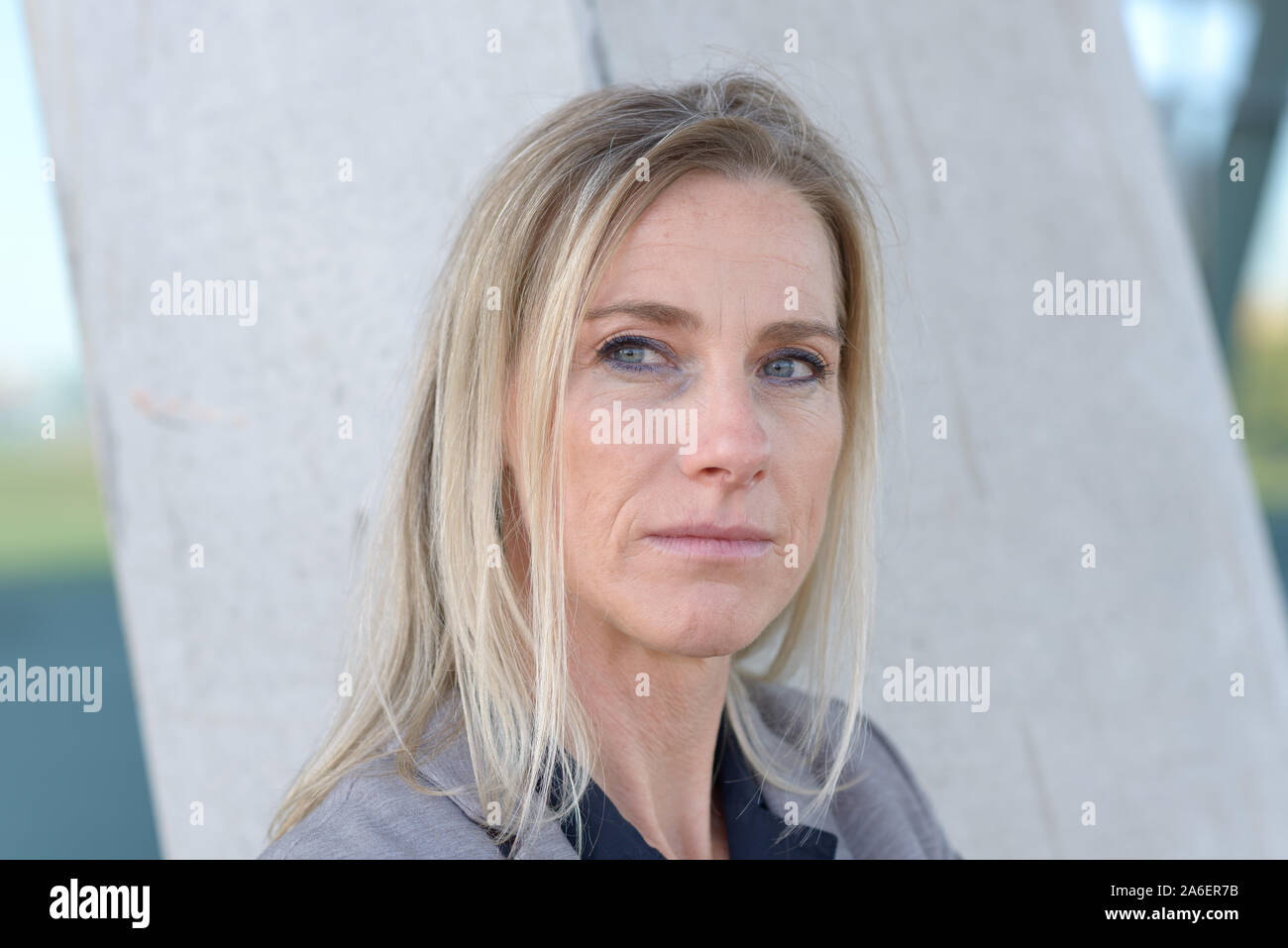 Middle-aged blond woman deep in thought standing staring to the side with a serious pensive expression in a close up portrait outdoors Stock Photo