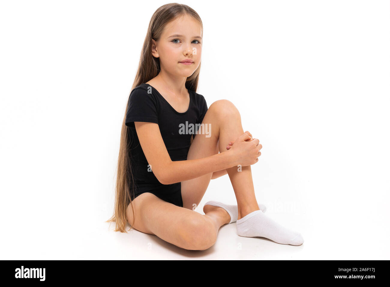 Picture of a gymnast girl sits in white short socks and black trico full height isolated on a white background Stock Photo