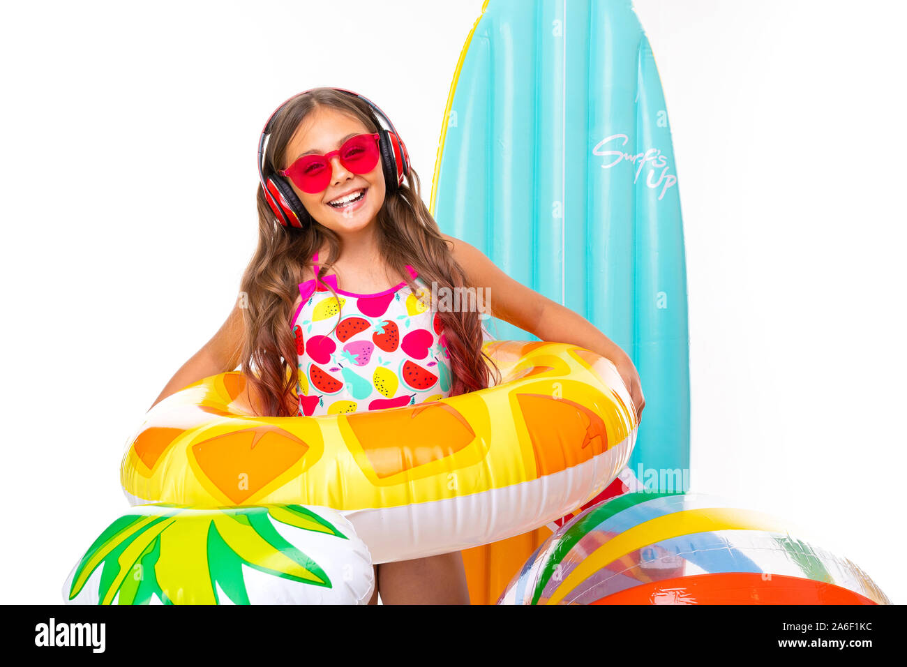 cool girl with long crucified hair in sunglasses and swimsuit stands near inflatable mattresses in a rubber ring smiles Stock Photo