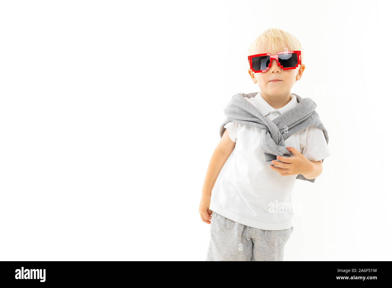 A little boy with short blonde hair, blue eyes, cute appearance, in a white  coat around his neck, grey pants, grey cap, glasses from a game with a red  Stock Photo -