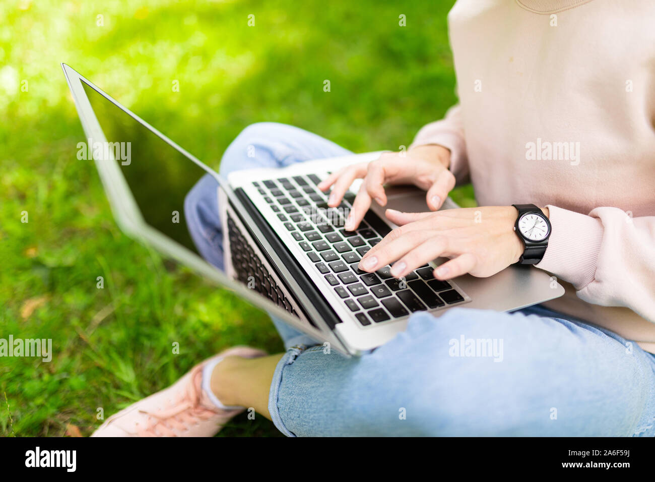 Young caucasian woman with perfect smile, plump lips, glasses walks in nature, sits on a grass with laptop and communicated with friends or works Stock Photo
