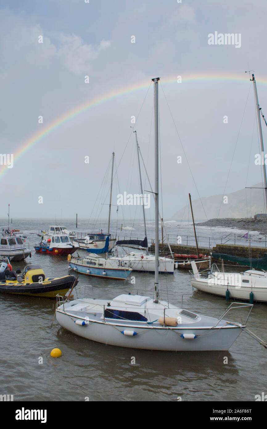 rainbow over the sea, boats, harbour and headland at Lynmouth during stormy weather, Devon, UK, September. Hight tide, Stock Photo