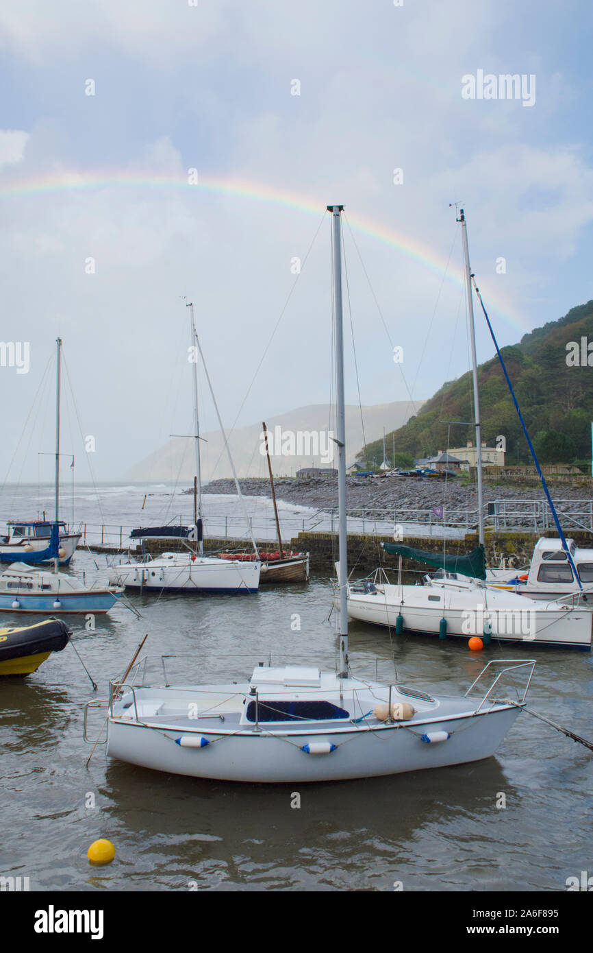rainbow over the sea, boats, harbour and headland at Lynmouth during stormy weather, Devon, UK, September. Hight tide,, Stock Photo