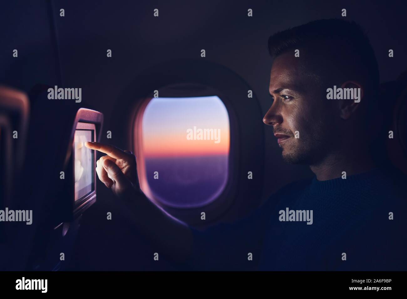 Man travel by airplane during night. Passenger using in-flight entertainment system and internet connection. Stock Photo