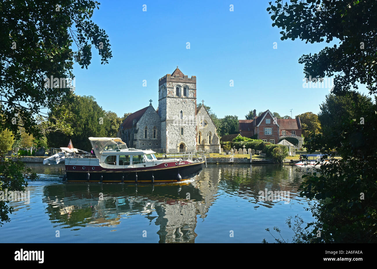 Berks - river Thames - summer day - river cruiser passing  Bisham church - reflections in the water -  sunlight - blue sky - picturesque Stock Photo