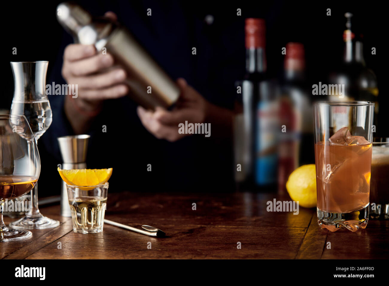 Barman mixing cocktails in a martini shaker behind a bar counter with assorted cocktails in