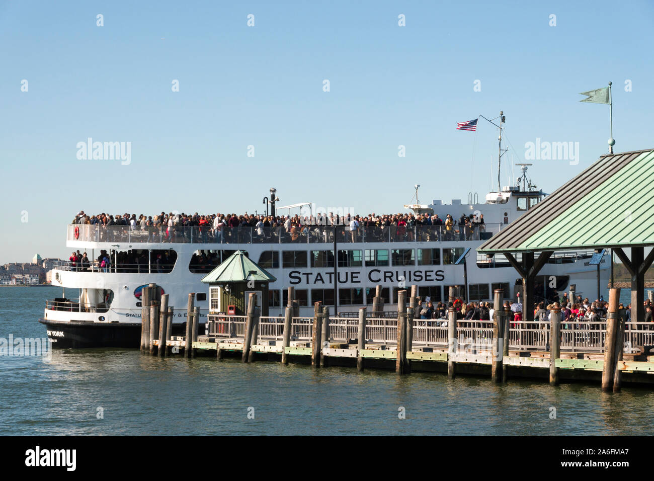Ferry to Ellis Island Tour Boat Filled with Tourists Arrives at Dock at Liberty Island Pier, NYC 
