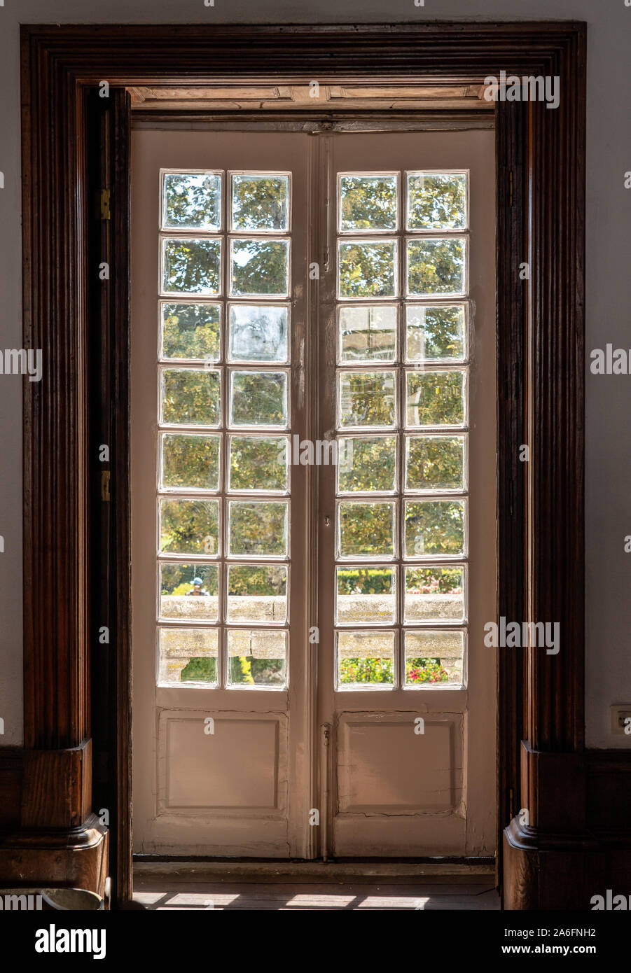 Wooden carved and glazed doors leading from old house into garden with sunlight Stock Photo