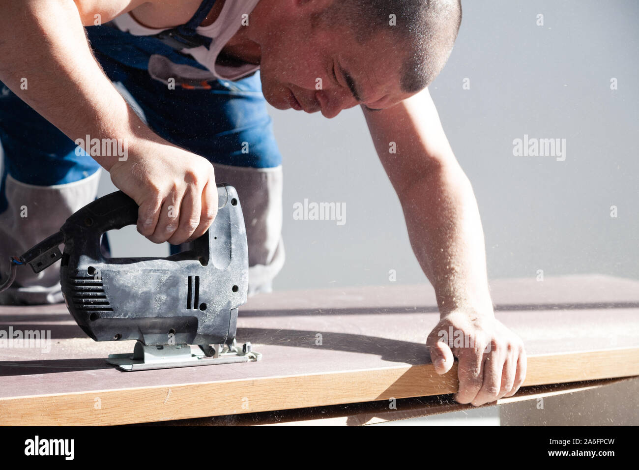 Closeup hand of carpenter, woodworker with professional cutting tool fretsaw or jigsaw, cut wooden tabletop, sawing plank, brown filings, sawdust. Con Stock Photo