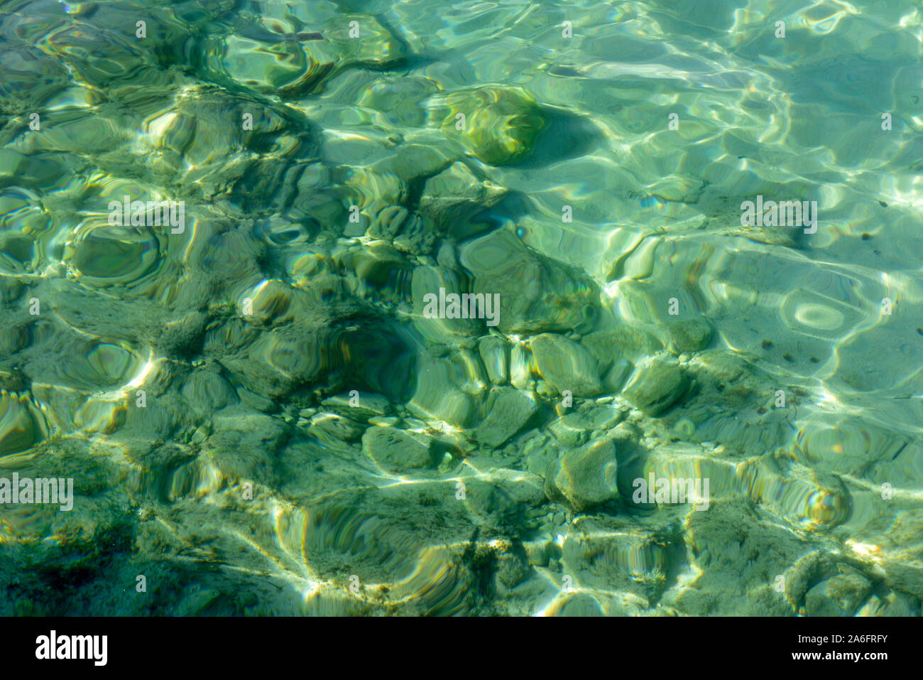 Dappled light patterns in clear green rippling sea water with distorted view of rocks on bottom Stock Photo