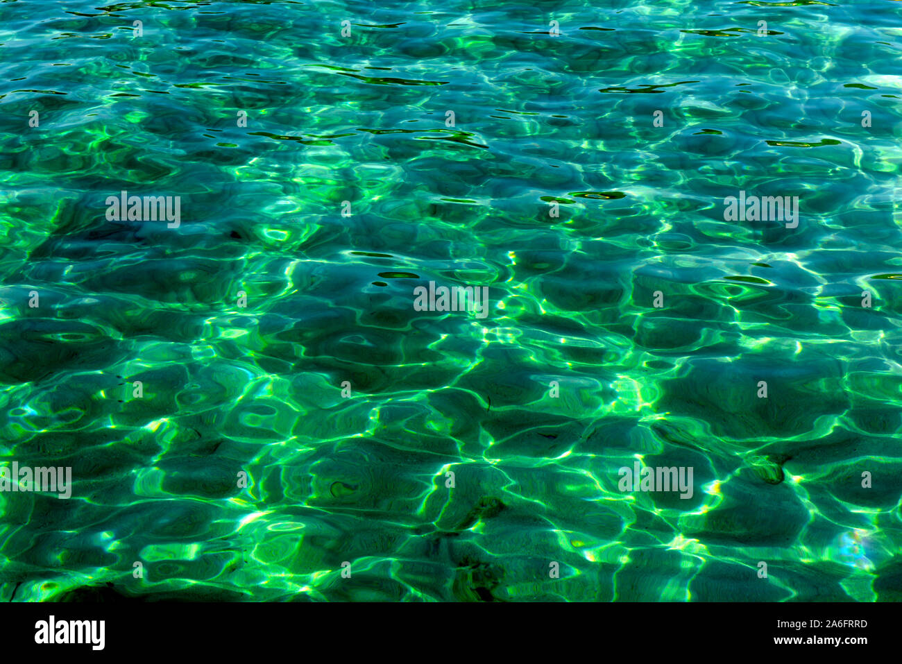 Dappled light patterns in clear green rippling sea water with distorted view of rocks on bottom Stock Photo