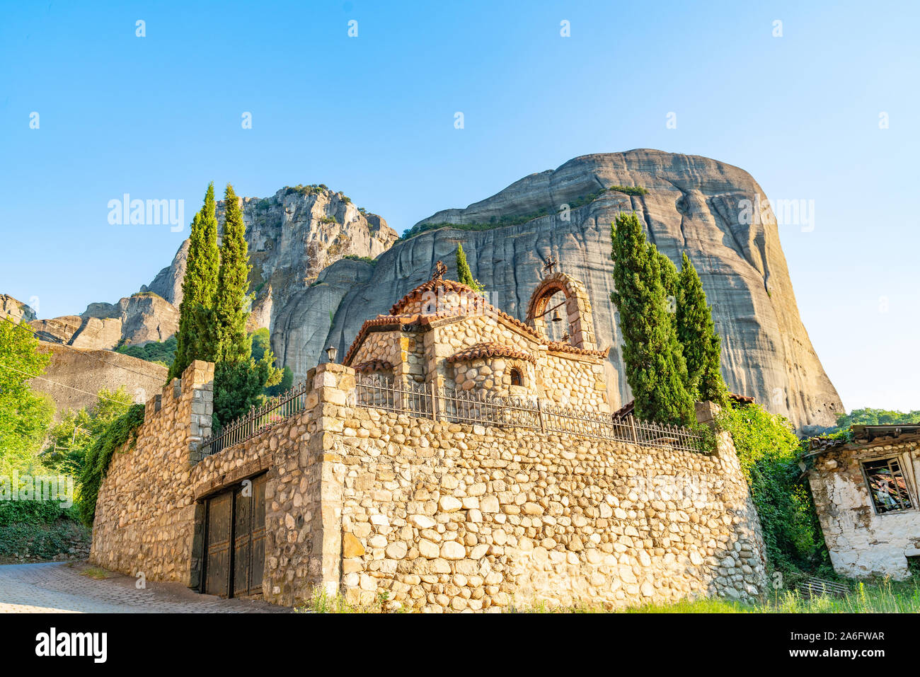 Large imposing rocks rise behind quaint Greek Orthodox stone church in town of Kastraki, Meteora Greece. Stock Photo