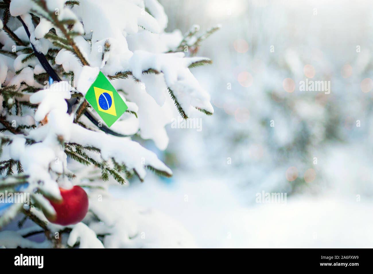 Christmas Brazil. Xmas tree covered with snow, decorations and a flag of Brazil. Snowy forest background in winter. Christmas greeting card. Stock Photo
