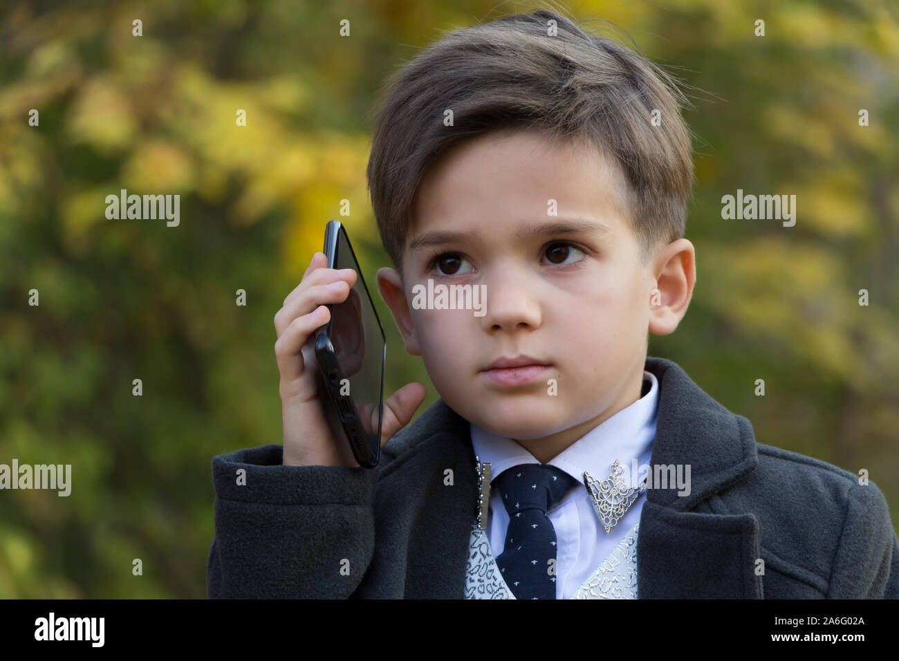 Portrait of pensive little businessman talking by phone on autumn background. The development of modern children concept. Little adults. A small man Stock Photo