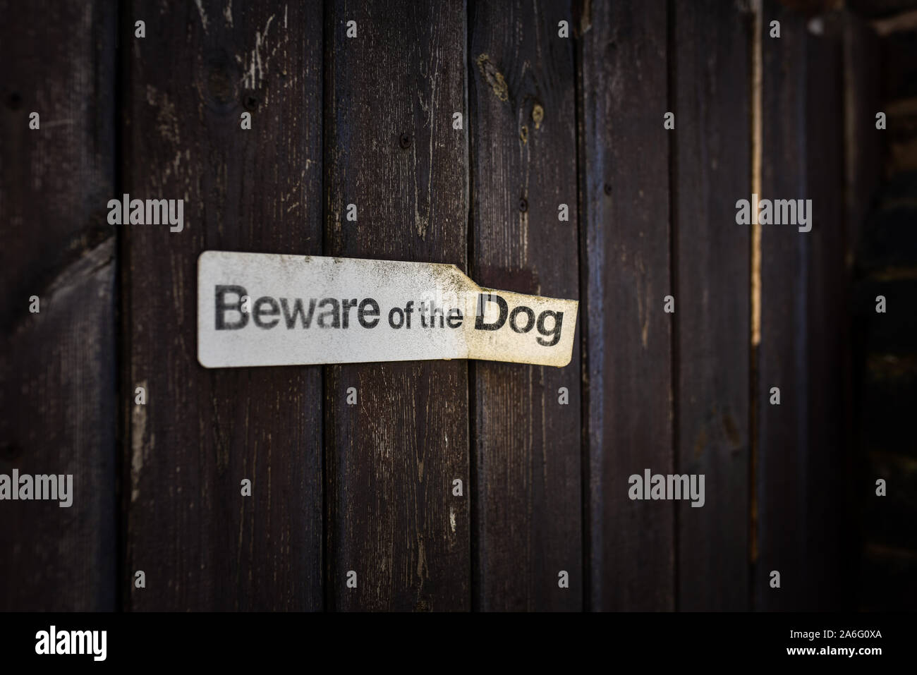 Beware of dog sign in disrepair nearly falling off the wooden fence, guard dog alert Stock Photo