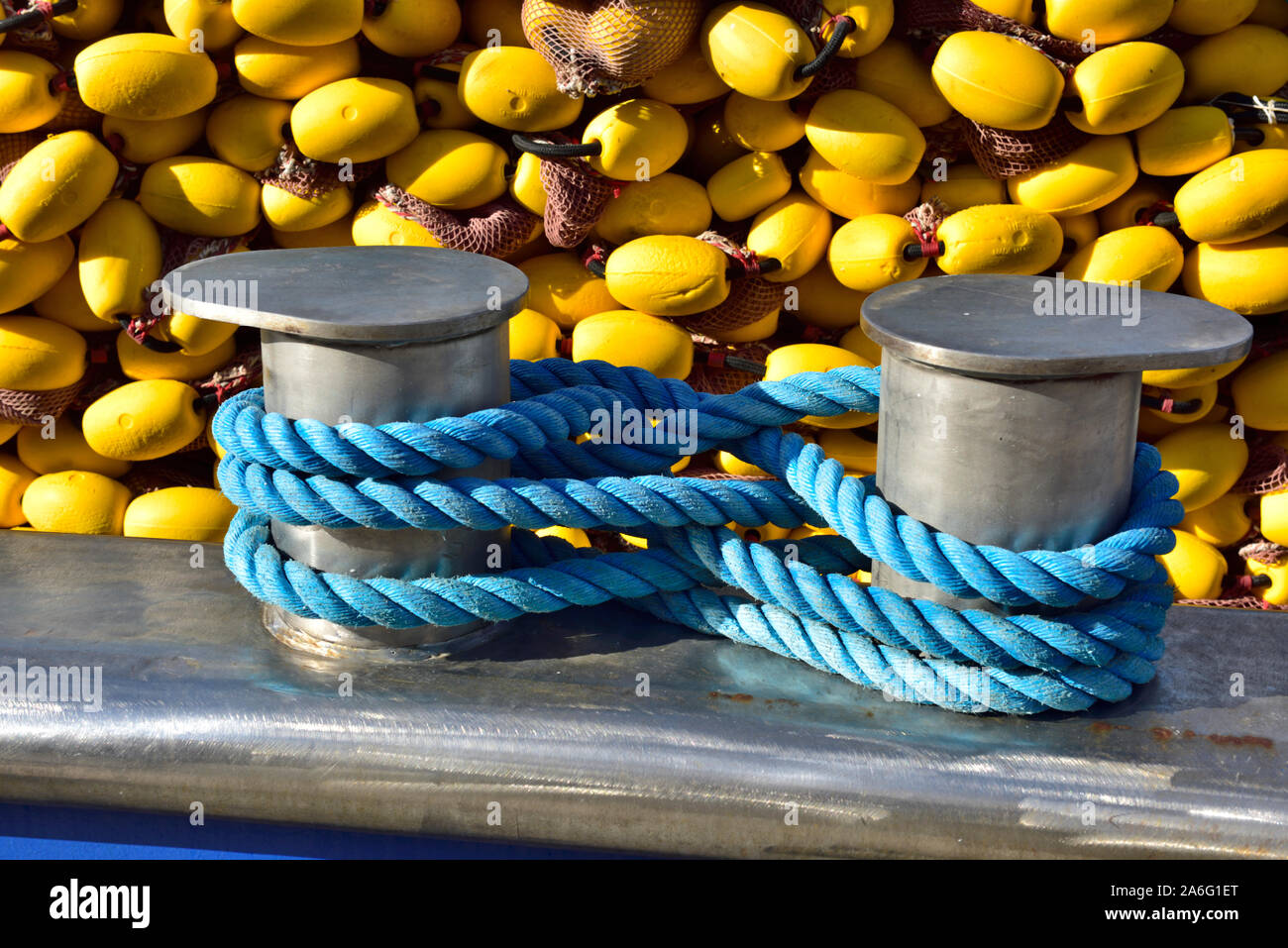 Mooring rope wrapped around stainless steel bollard on gunwale of fishing boat with net and floats behind Stock Photo
