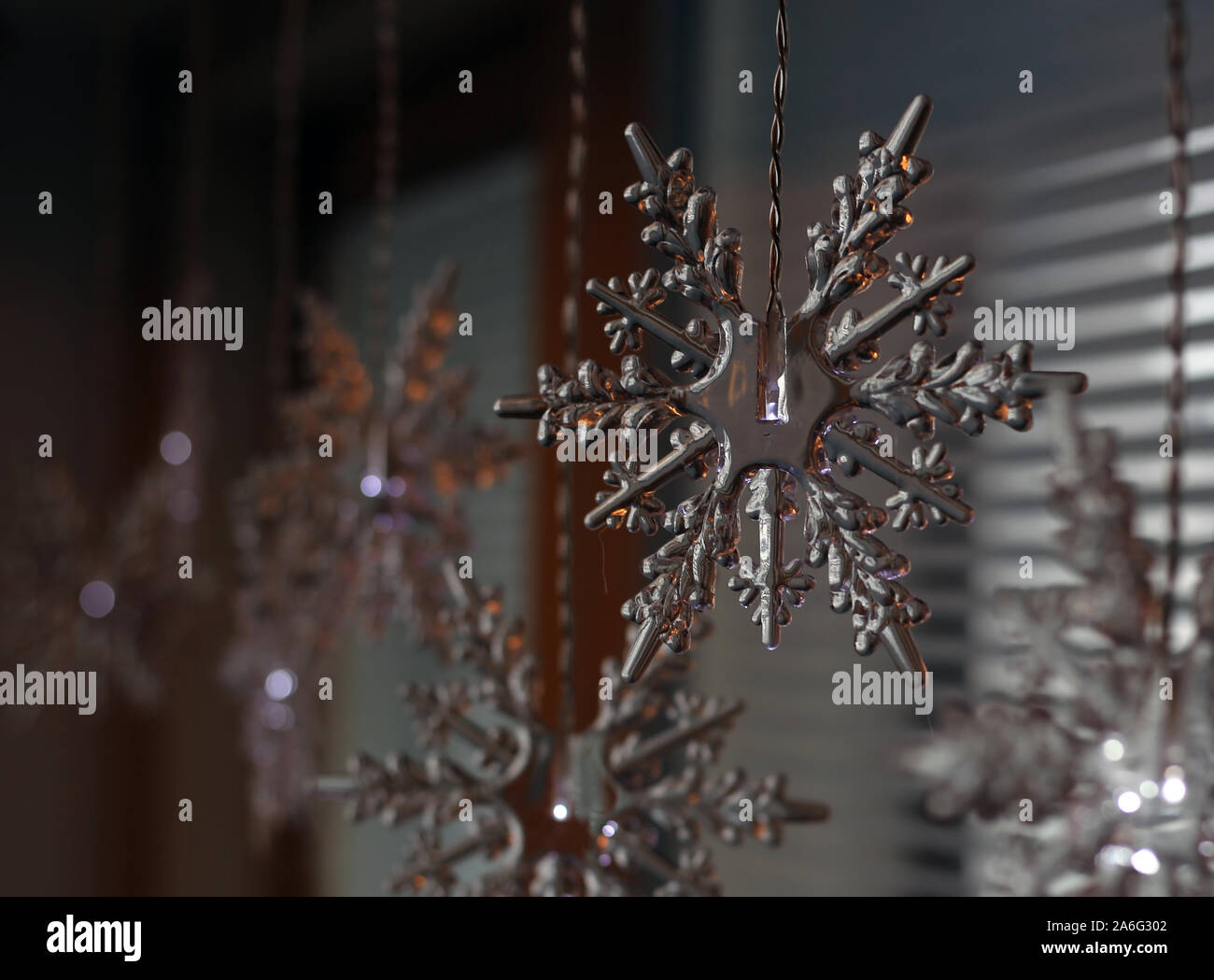 Snowflake shaped Christmas lights hanging in front of a window indoors. Lovely piece of winter / holiday season themed home decoration. Stock Photo