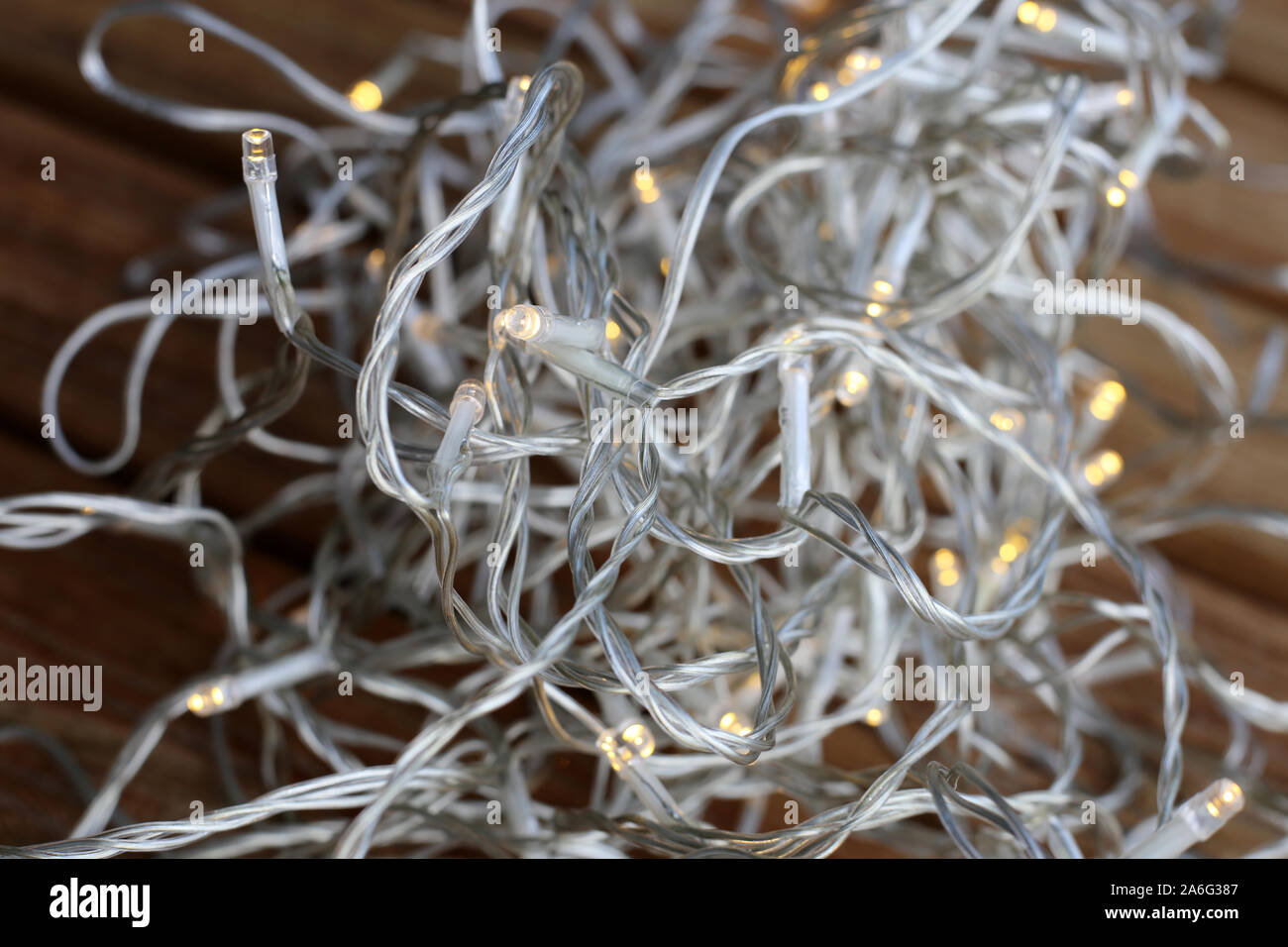 Christmas light string pile on a wooden floor. The string is transparent and the lights are small, light yellow led bulbs. Energy efficient LEDs! Stock Photo