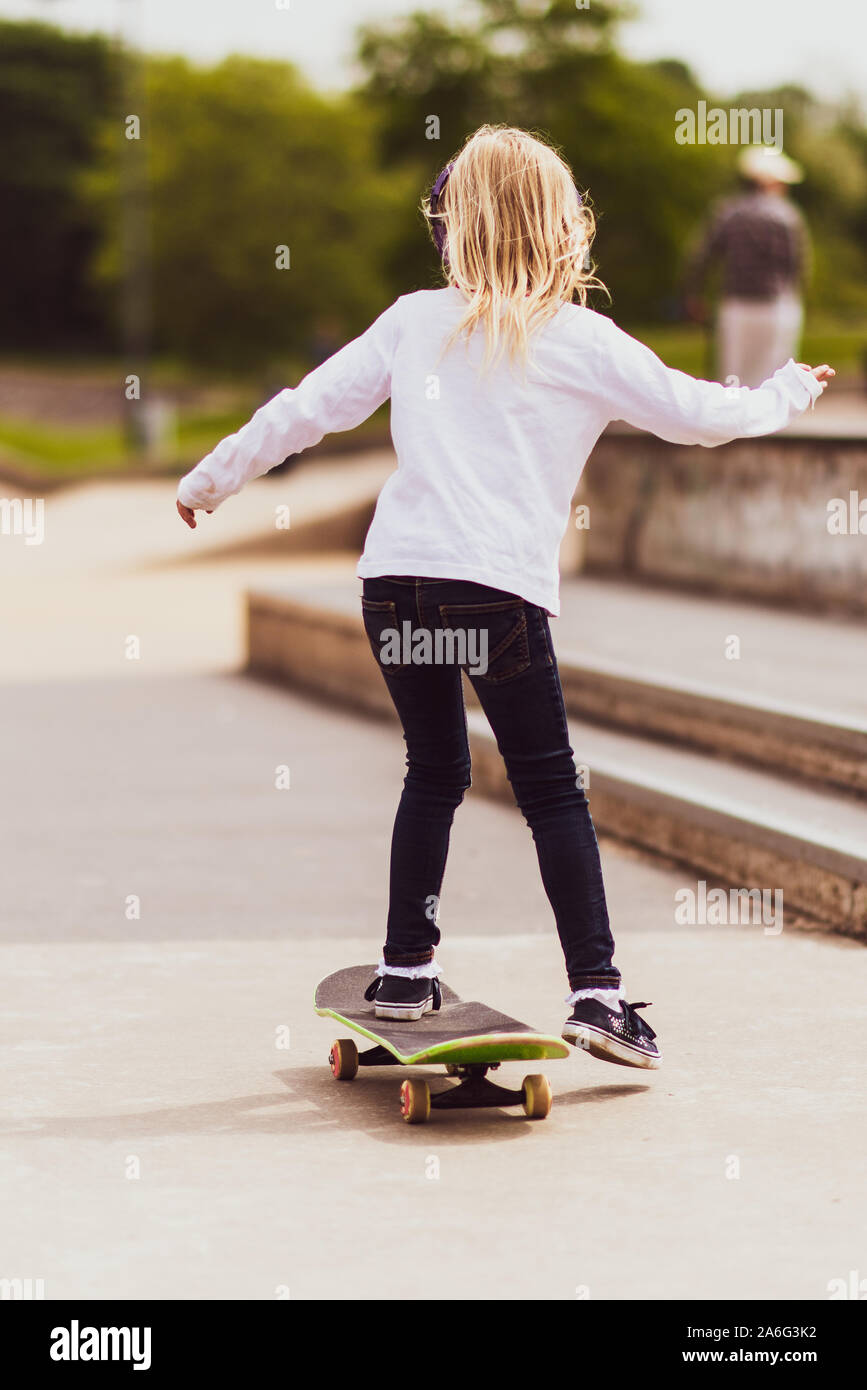 A pretty little girl with blonde hair at the local skateboard park  practicing and riding around on her skateboard while listening to music  Stock Photo - Alamy