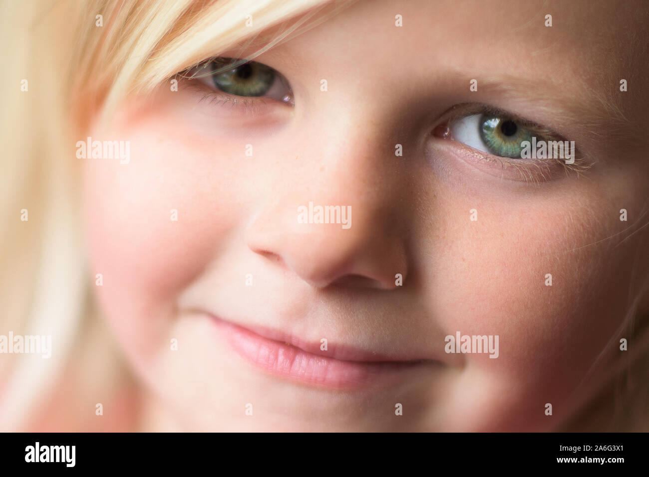 A beautiful little blonde girl with bright green eyes smiling into the camera, close up Stock Photo
