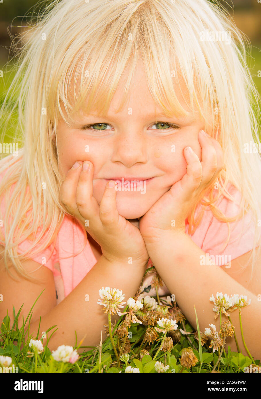 A pretty little girl with blonde hair and bright green eyes lying on the  grass near some daisy's, daisies Stock Photo - Alamy