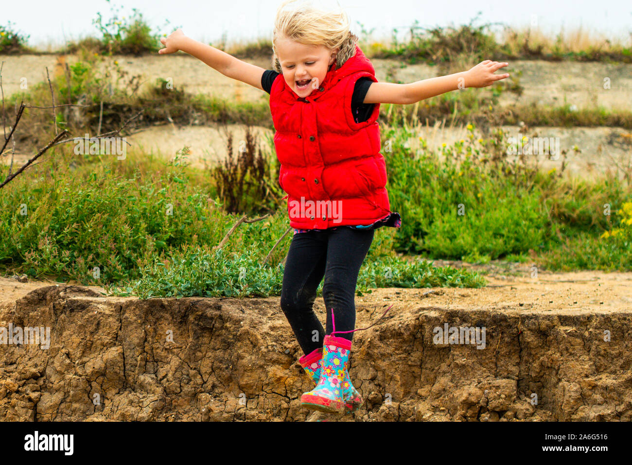 A cute little girl in a red coat jumping off the cliffs onto the sand