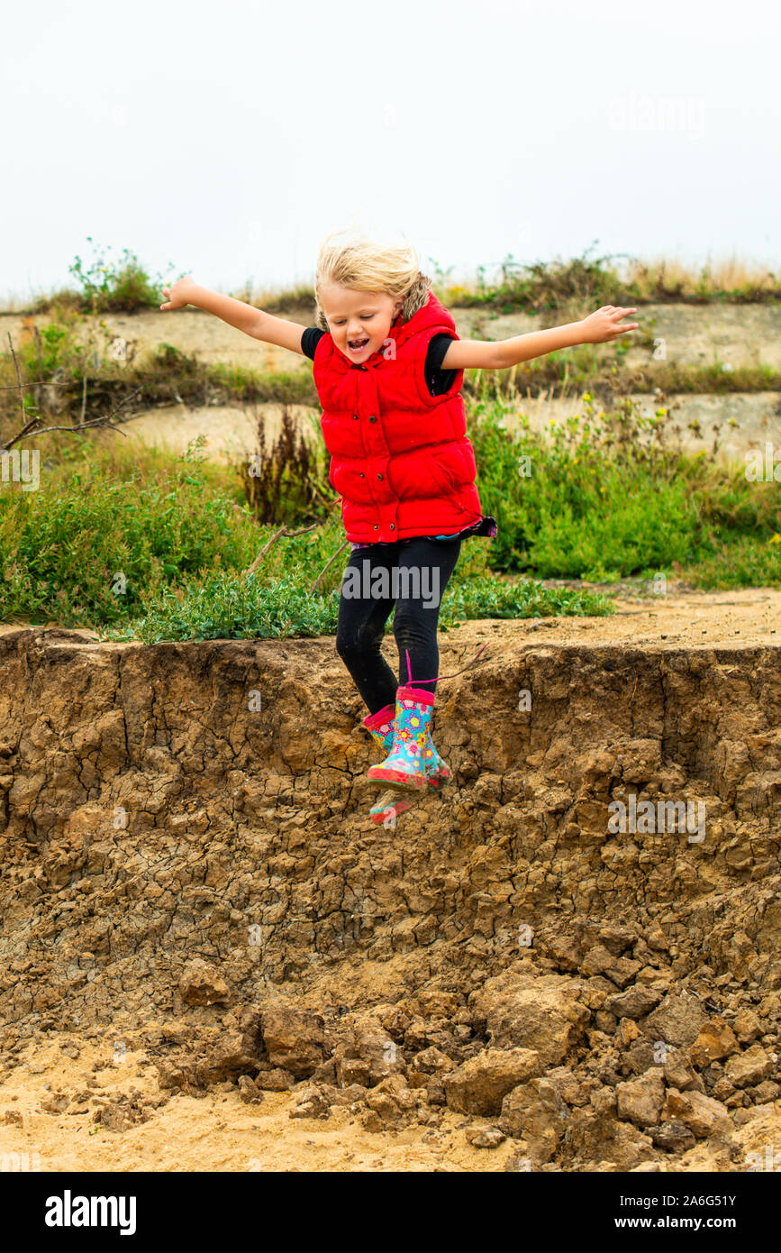 A cute little girl in a red coat jumping off the cliffs onto the sand