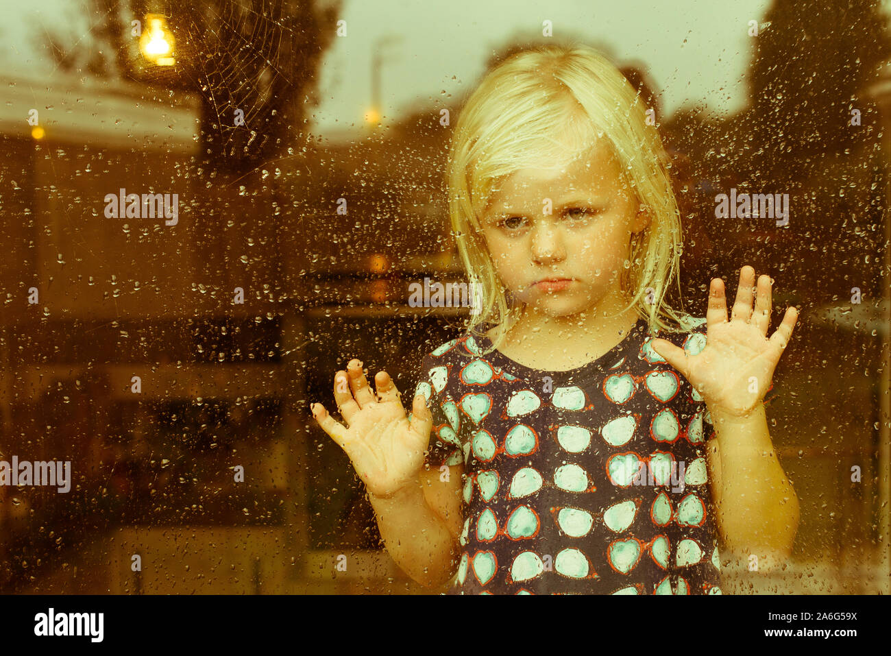 A gorgeous, pretty little girl staring out of the window on a wet, cold ...