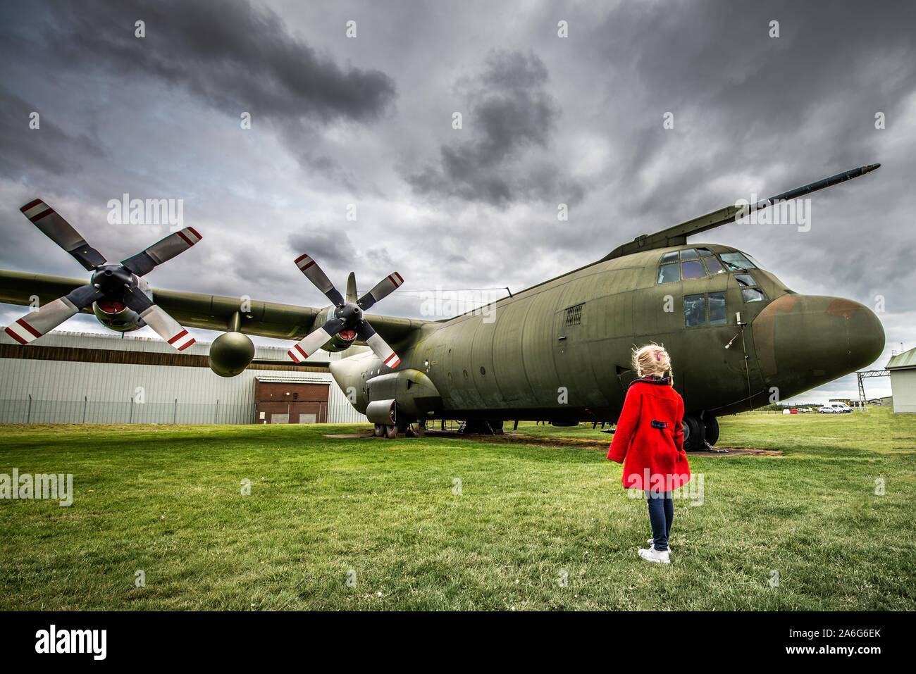 A little girl in a red coat visits an airbase and stares in awe at a ...