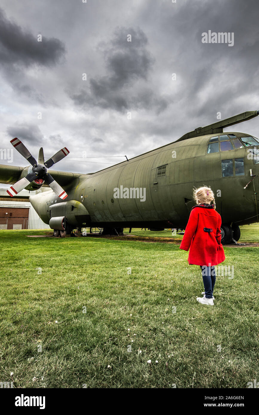 A little girl in a red coat visits an airbase and stares in awe at a ...