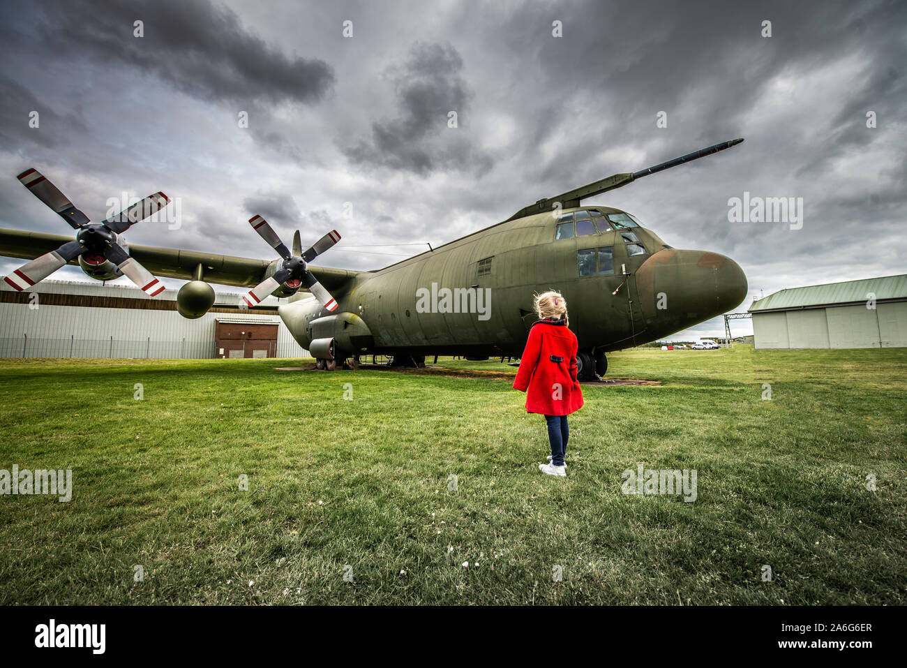 A little girl in a red coat visits an airbase and stares in awe at a ...
