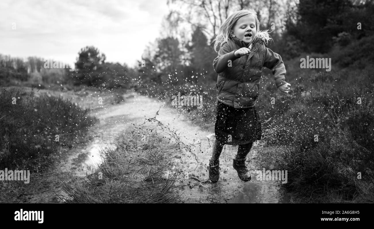 A little girl has fun out walking in the countryside hiking, puddle jumping and climbing in the cold autumn weather Stock Photo