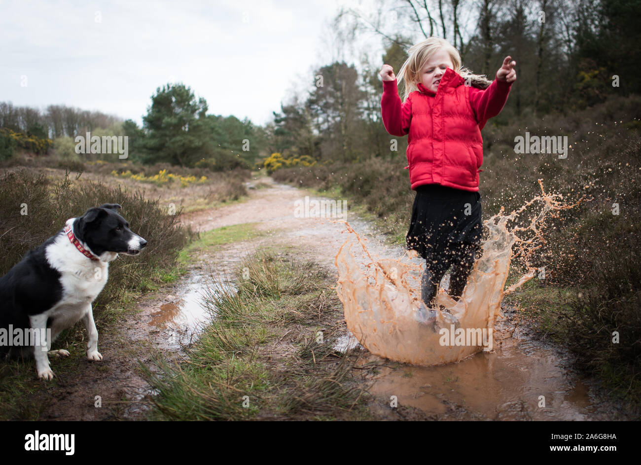 Pretty little girl jumping in very muddy puddle playing with her pet